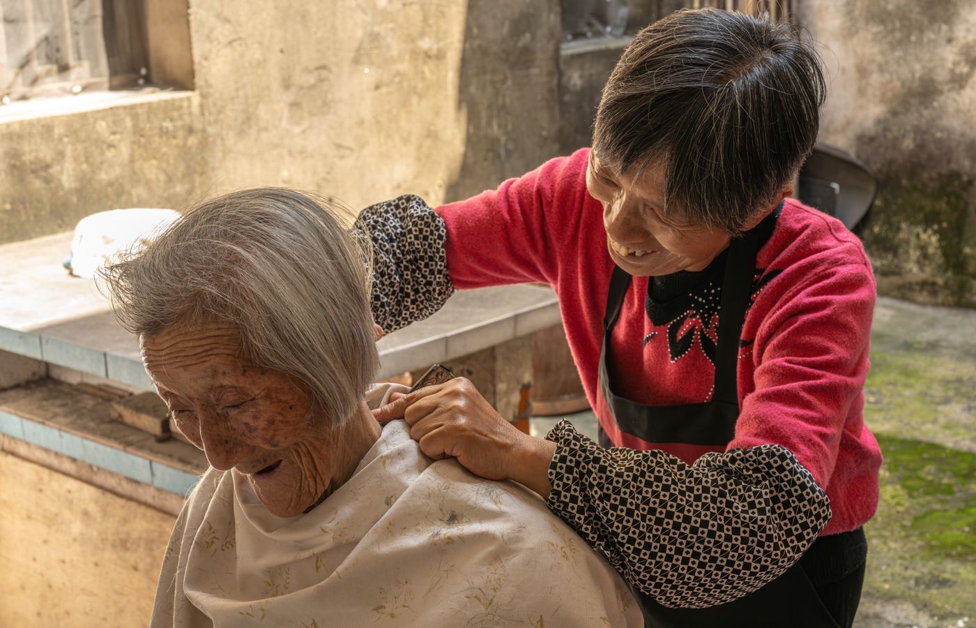 An older woman having her hair brushed outdoors by a family member