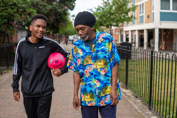A helper walking outdoors beside an older adult
