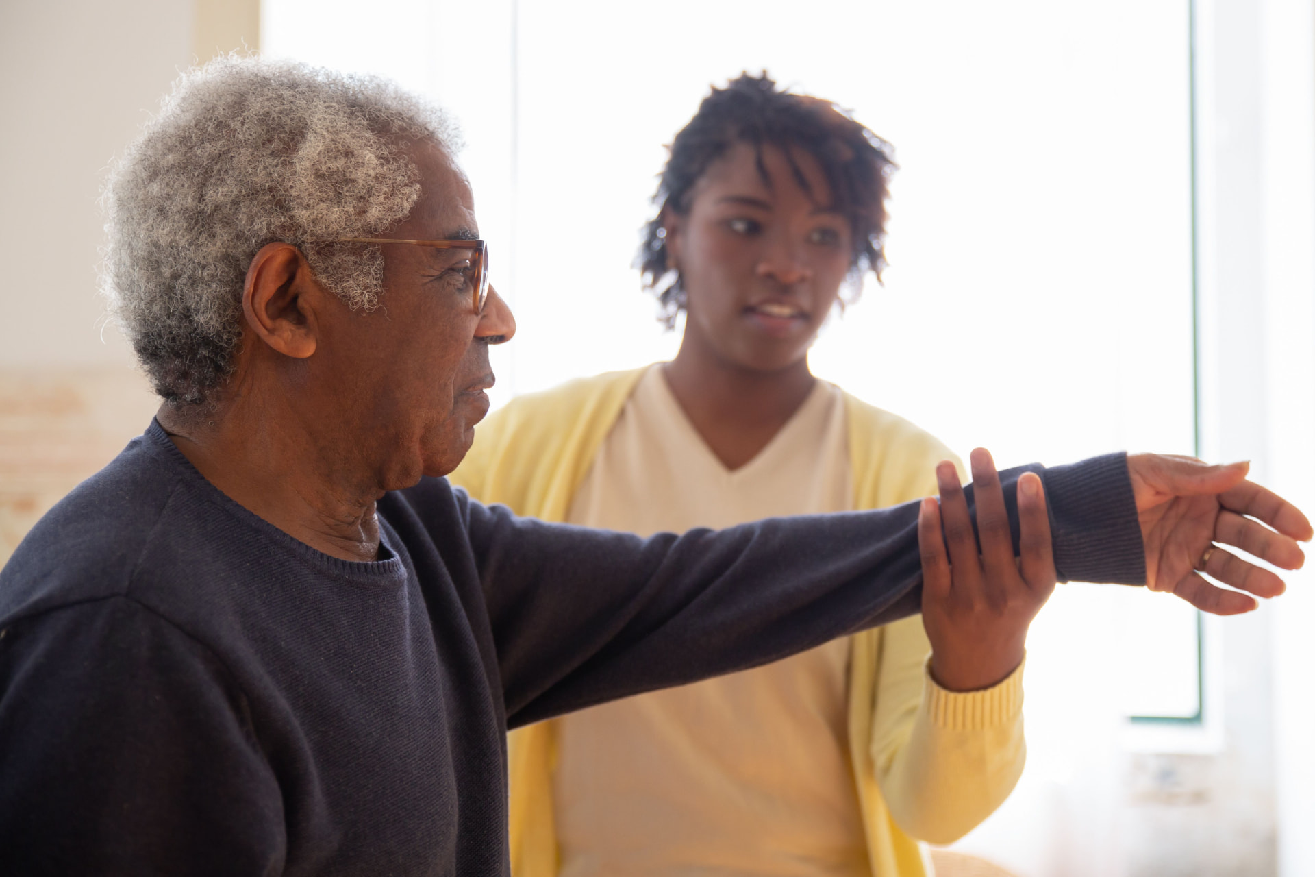 A caregiver guiding an older man through gentle arm stretches at home