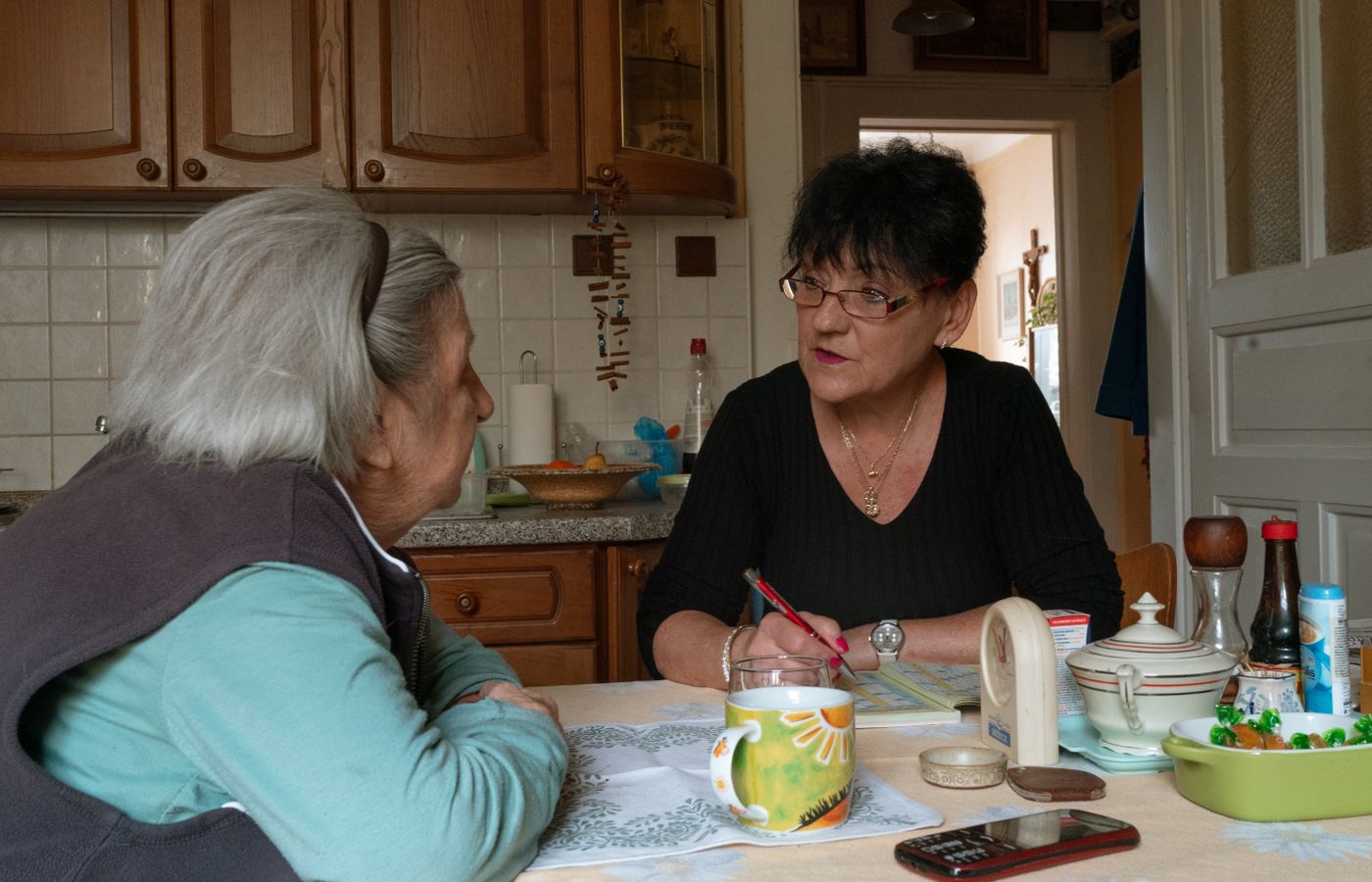 A caregiver chatting with an older woman across her kitchen table