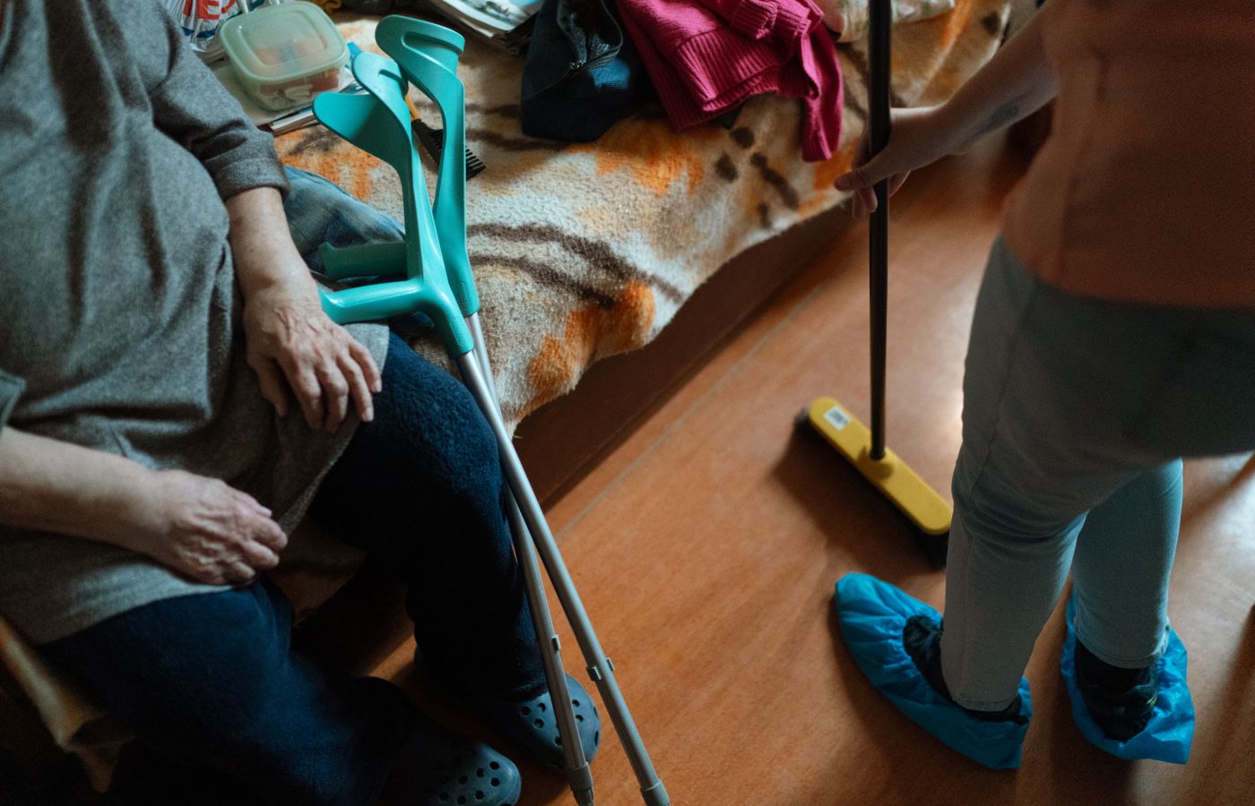 A helper mopping the floor while an older adult rests nearby