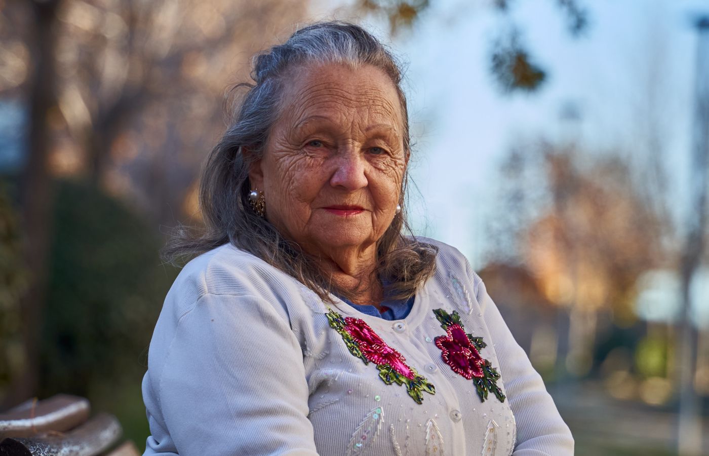 An older woman resting on a park bench in autumn light